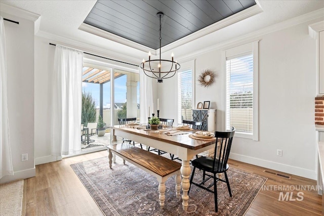 dining space featuring light wood-style floors, visible vents, a tray ceiling, and crown molding