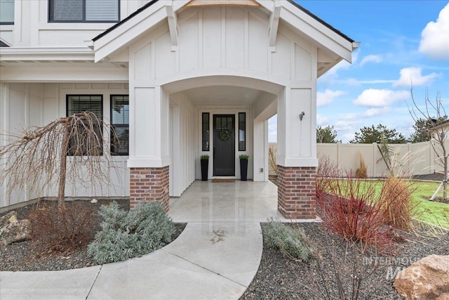 entrance to property with board and batten siding, covered porch, brick siding, and fence