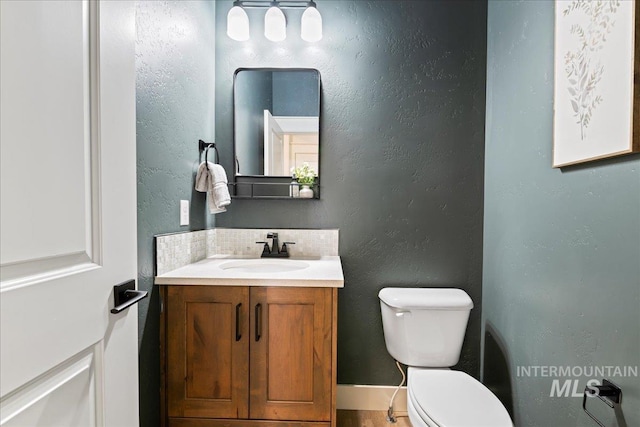 half bath with a textured wall, vanity, and toilet