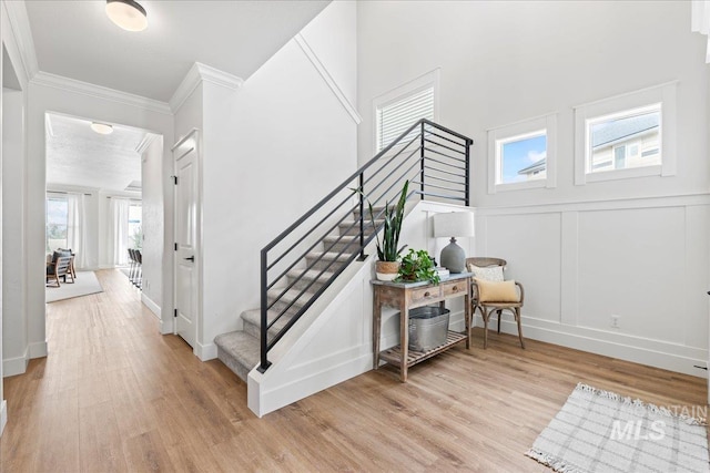 stairway with ornamental molding, wood finished floors, and a decorative wall