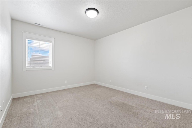 spare room with carpet floors, baseboards, visible vents, and a textured ceiling