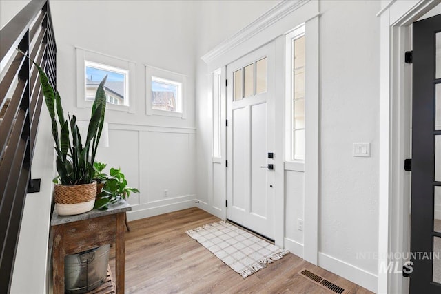 entryway featuring light wood finished floors, baseboards, visible vents, and a decorative wall