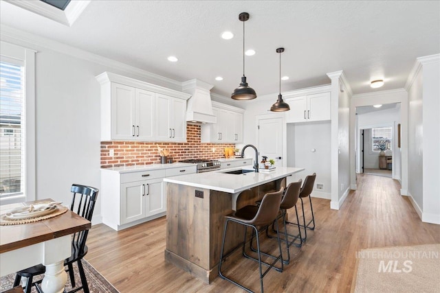 kitchen with a sink, light countertops, stainless steel gas range, backsplash, and crown molding