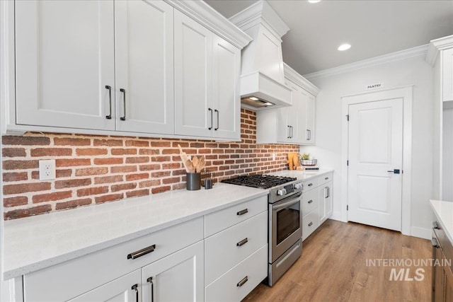 kitchen featuring stainless steel gas stove, tasteful backsplash, white cabinets, ornamental molding, and light stone countertops