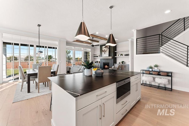 811 N Creekwater Lot 13/6, Eagle, ID 83616 - kitchen featuring stainless steel microwave, dark countertops, light wood-type flooring, a lit fireplace, and recessed lighting