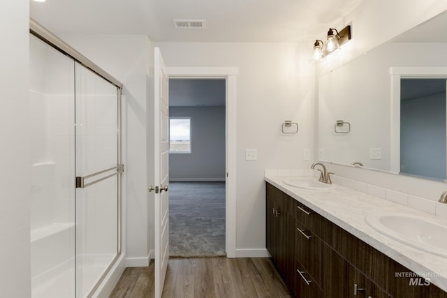 full bathroom with double vanity, a shower with door, a sink, and wood finished floors