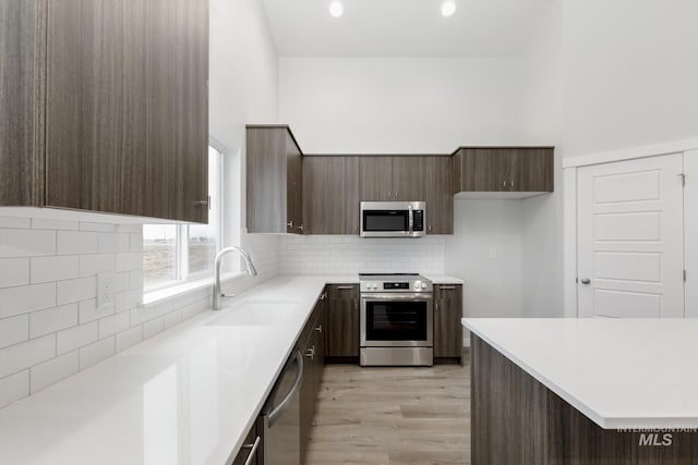 kitchen featuring light countertops, decorative backsplash, appliances with stainless steel finishes, light wood-style floors, and a sink