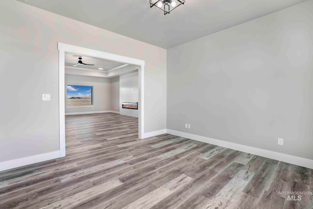 empty room featuring ceiling fan, a raised ceiling, and wood-type flooring