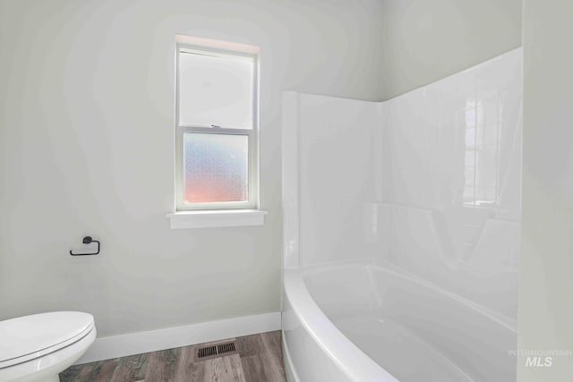 bathroom with toilet, wood-type flooring, and washtub / shower combination