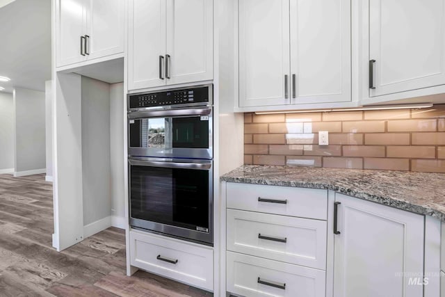 kitchen featuring hardwood / wood-style floors, backsplash, white cabinetry, double oven, and light stone counters