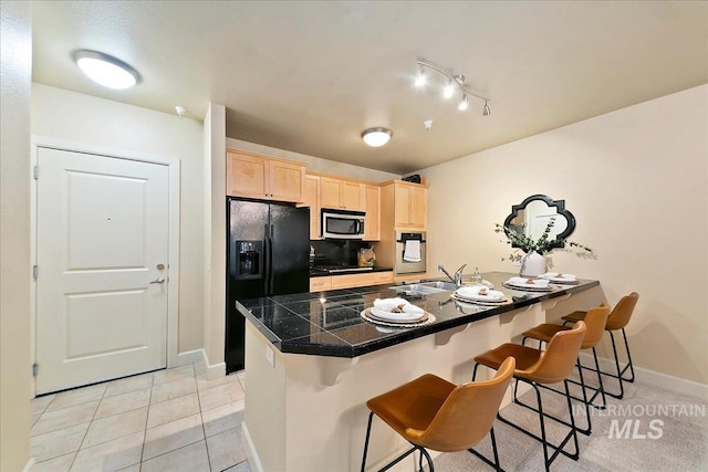 kitchen featuring light brown cabinetry, sink, light tile patterned flooring, black appliances, and a breakfast bar area