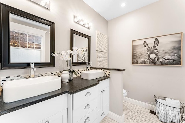 bathroom with double vanity, toilet, baseboards, and a sink