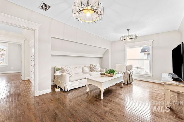 living area with hardwood / wood-style floors, baseboards, visible vents, and a notable chandelier