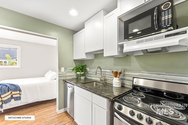 kitchen with dark stone counters, a sink, stainless steel appliances, light wood-style flooring, and white cabinets