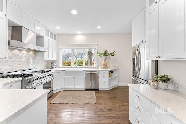 kitchen featuring wall chimney exhaust hood, stainless steel appliances, white cabinetry, and light stone counters