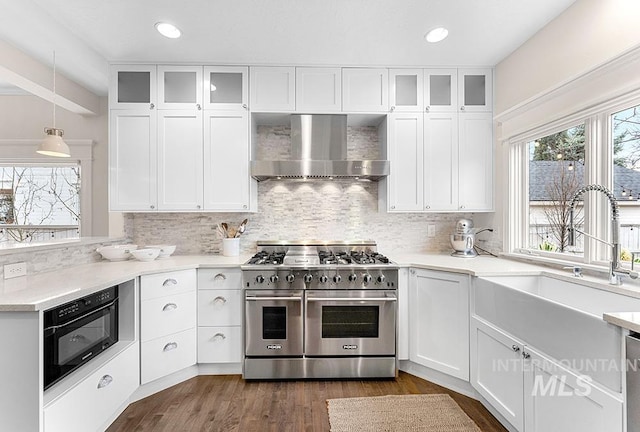 kitchen featuring tasteful backsplash, a sink, double oven range, wall chimney exhaust hood, and white cabinetry