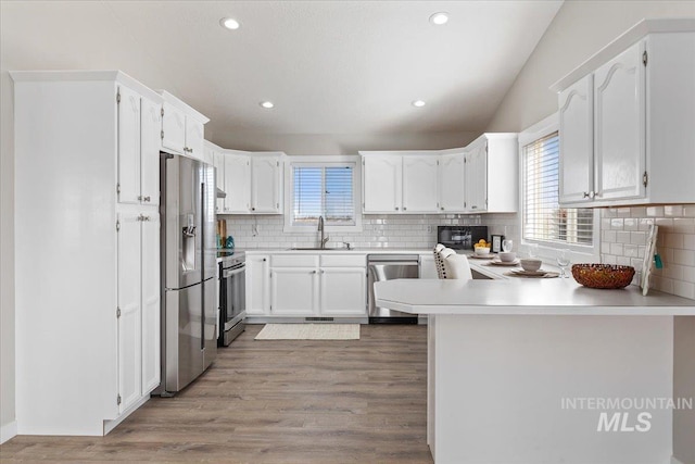 kitchen with a sink, stainless steel appliances, light wood-style floors, and a peninsula