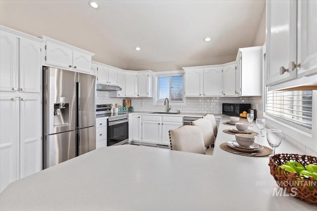 kitchen featuring under cabinet range hood, vaulted ceiling, decorative backsplash, appliances with stainless steel finishes, and a sink