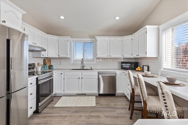 kitchen featuring lofted ceiling, a sink, white cabinets, under cabinet range hood, and appliances with stainless steel finishes