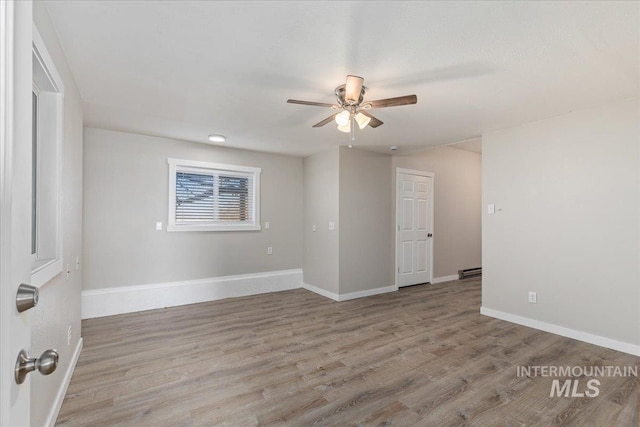 unfurnished room with a baseboard radiator, wood finished floors, baseboards, and ceiling fan