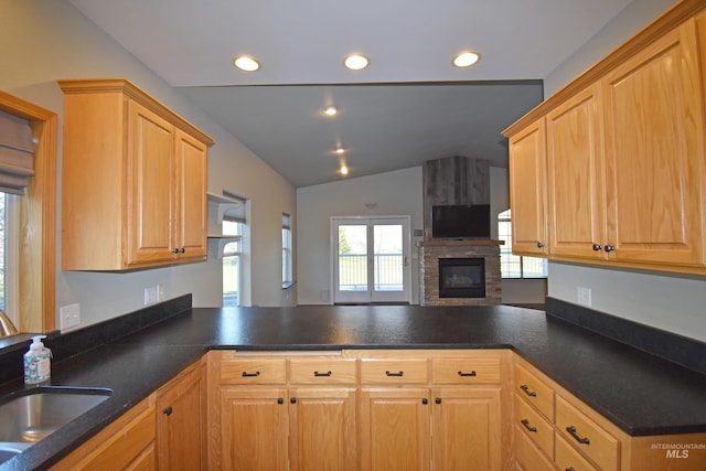 kitchen featuring sink, lofted ceiling, kitchen peninsula, and a stone fireplace