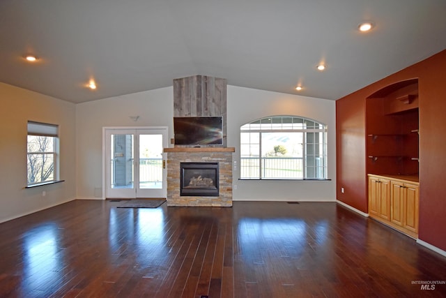 unfurnished living room with built in features, vaulted ceiling, a stone fireplace, and dark wood-type flooring