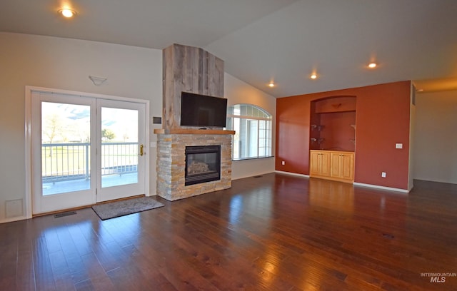 unfurnished living room featuring built in features, dark hardwood / wood-style floors, vaulted ceiling, and a stone fireplace