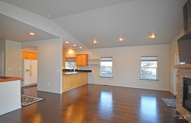 unfurnished living room featuring sink, dark hardwood / wood-style flooring, lofted ceiling, and a stone fireplace