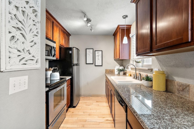 kitchen featuring a textured ceiling, light wood-type flooring, stainless steel appliances, sink, and decorative light fixtures