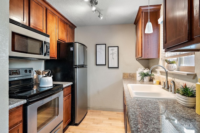 kitchen with appliances with stainless steel finishes, light wood-type flooring, dark stone countertops, sink, and decorative light fixtures