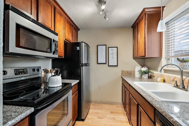 kitchen with hanging light fixtures, sink, light wood-type flooring, appliances with stainless steel finishes, and a textured ceiling