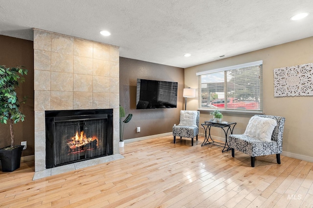 living area with a tiled fireplace, a textured ceiling, and light hardwood / wood-style flooring