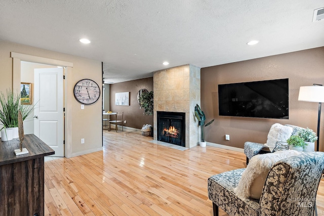 living room featuring a textured ceiling, a tiled fireplace, and light wood-type flooring