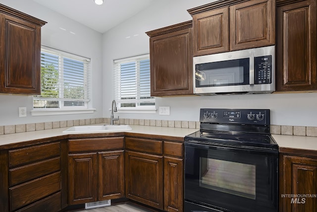 1030 Caswell Ave W, Twin Falls, ID 83301 - kitchen with black range with electric cooktop, stainless steel microwave, light countertops, dark brown cabinets, and vaulted ceiling