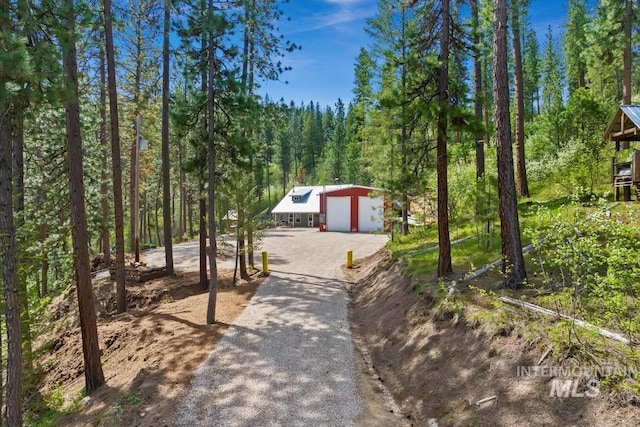 view of front of house featuring a forest view, gravel driveway, a detached garage, and an outdoor structure