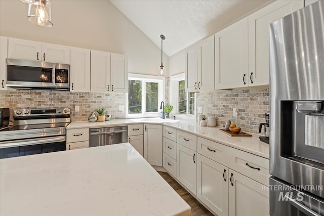 kitchen with stainless steel appliances, a sink, tasteful backsplash, white cabinets, and high vaulted ceiling