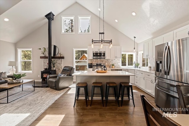 kitchen featuring appliances with stainless steel finishes, a wood stove, high vaulted ceiling, white cabinets, and a breakfast bar