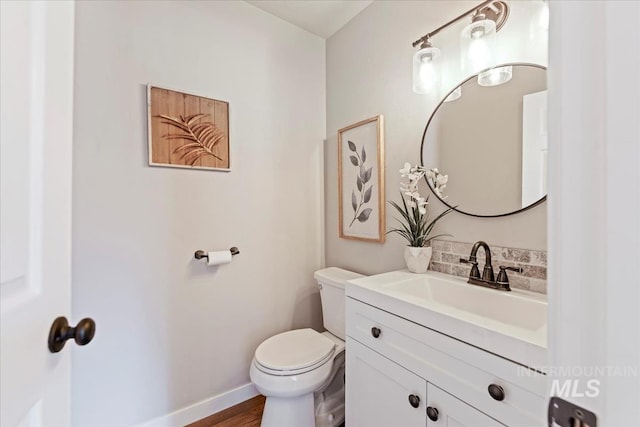 bathroom with toilet, vanity, baseboards, wood finished floors, and decorative backsplash