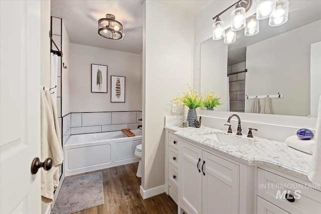bathroom with wood finished floors, toilet, vanity, and a bath