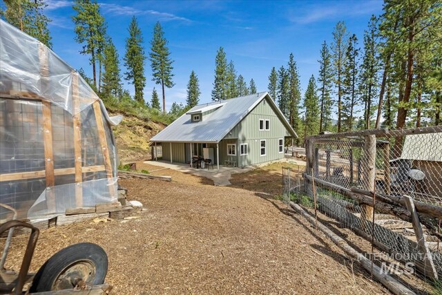 back of house featuring an exterior structure, an outdoor structure, board and batten siding, metal roof, and a patio