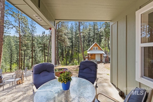 view of patio / terrace with outdoor dining space, a forest view, an outbuilding, and a storage unit