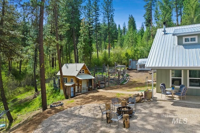 view of property exterior with an outdoor fire pit, metal roof, an outdoor structure, a patio area, and a wooded view