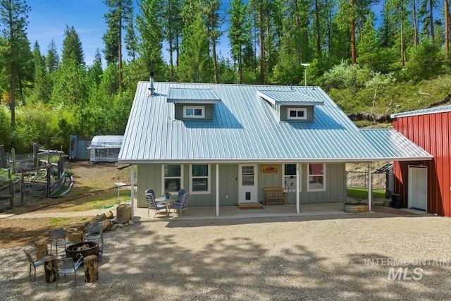back of property with an outdoor fire pit, board and batten siding, metal roof, and covered porch