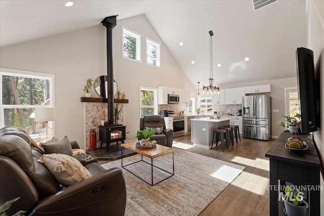 living area featuring a wood stove, high vaulted ceiling, wood finished floors, and recessed lighting