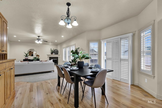 dining area featuring baseboards, light wood finished floors, recessed lighting, a fireplace, and ceiling fan with notable chandelier