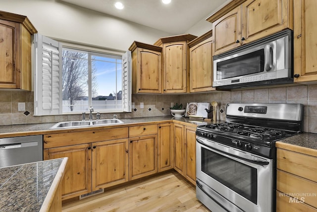 kitchen with a sink, stainless steel appliances, tasteful backsplash, and light wood-style floors