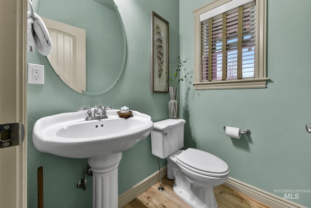 half bath featuring baseboards, toilet, and wood finished floors