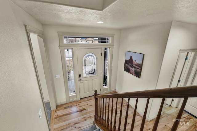 foyer with baseboards, light wood-type flooring, and a textured ceiling