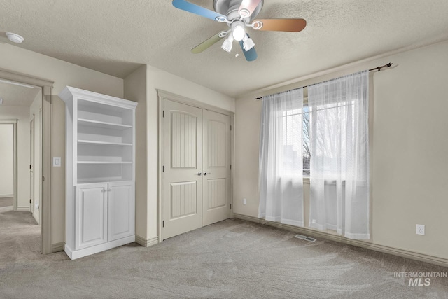 unfurnished bedroom with light carpet, visible vents, a textured ceiling, and a closet