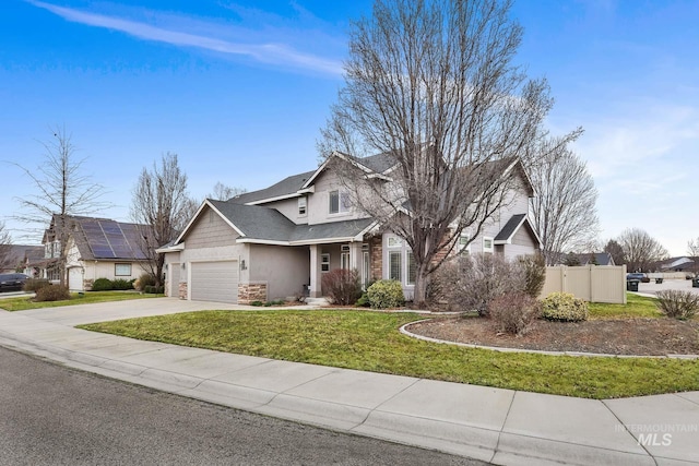 traditional-style house featuring stucco siding, driveway, stone siding, fence, and a front yard